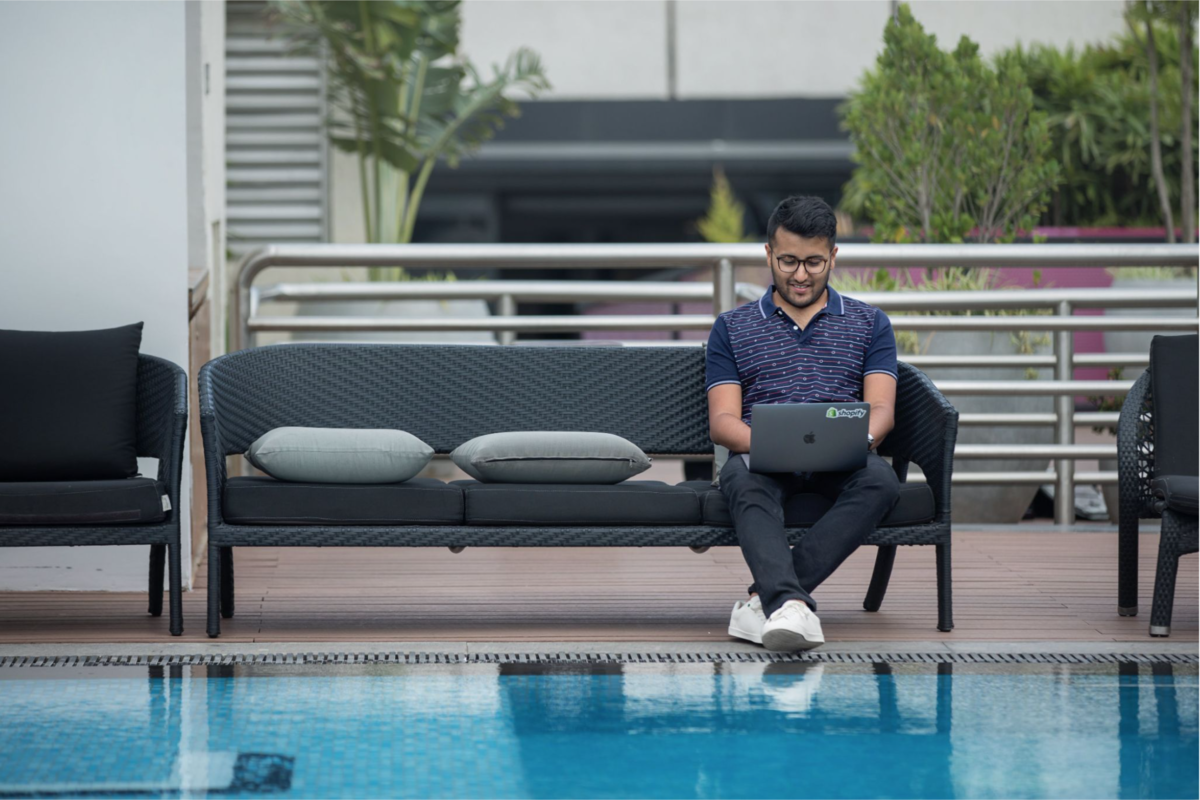 Young professional sitting by poolside while working on a laptop.