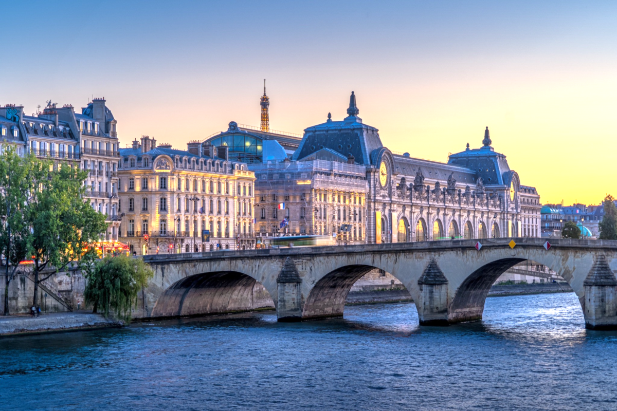 The Musée d'Orsay with a bridge and the Seine River in Paris at sunset.