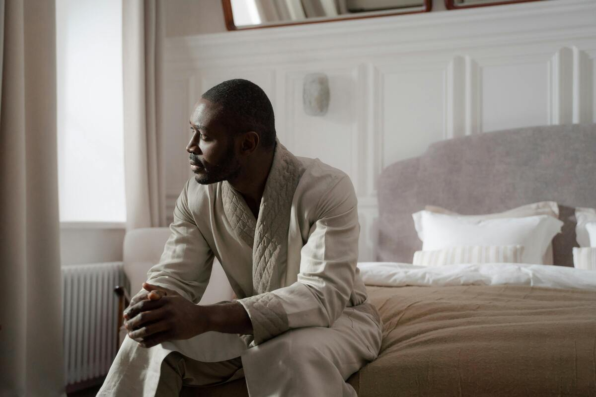 A man sitting on a hotel bed looking out a window.