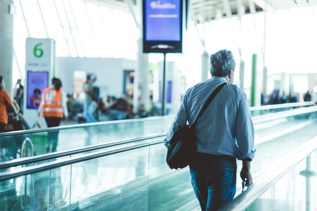 A man standing on the moving stairs at an airport.
