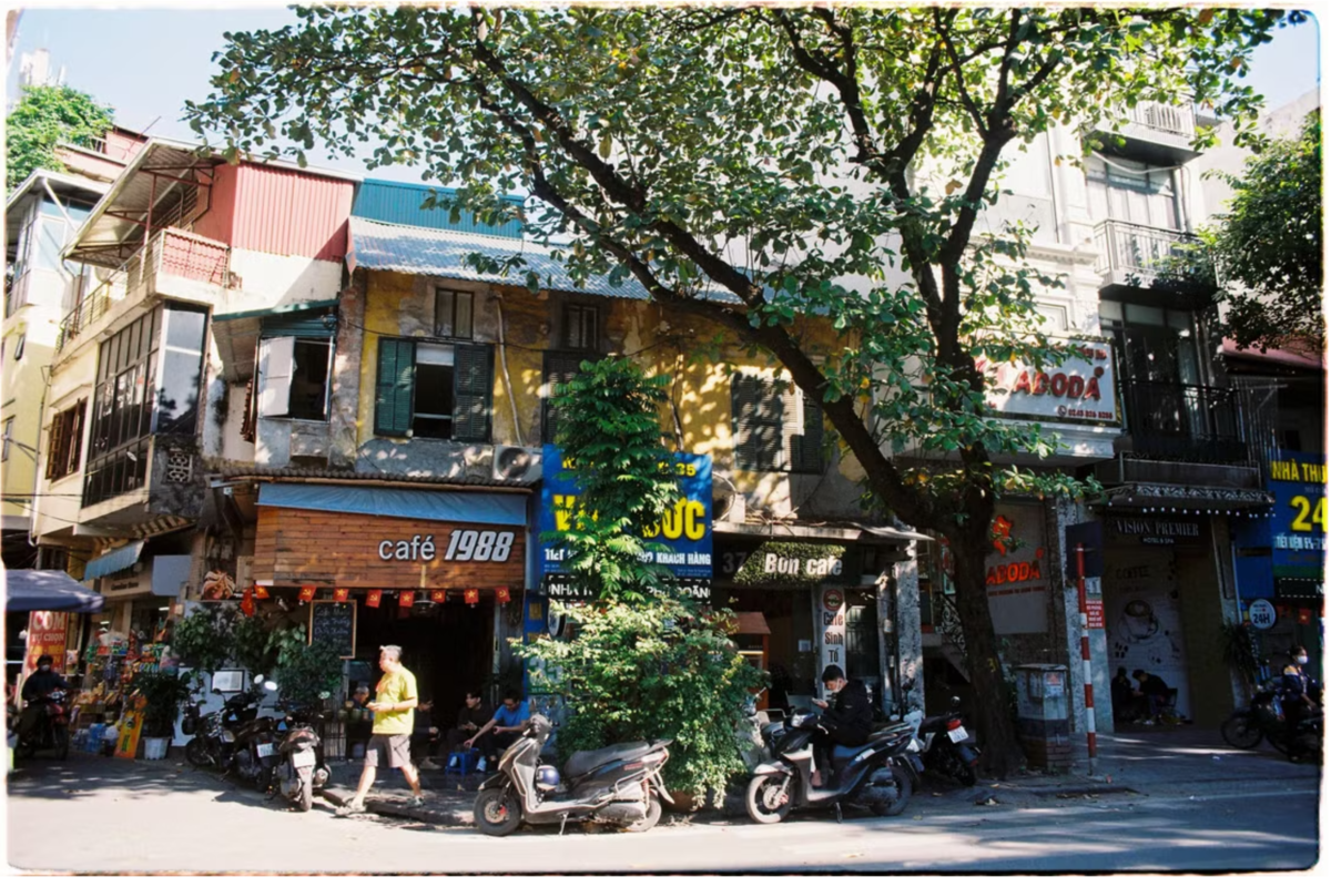 A busy sidewalk in Hanoi, Vietnam, with people parked on motorbikes in front of restaurants and stores.