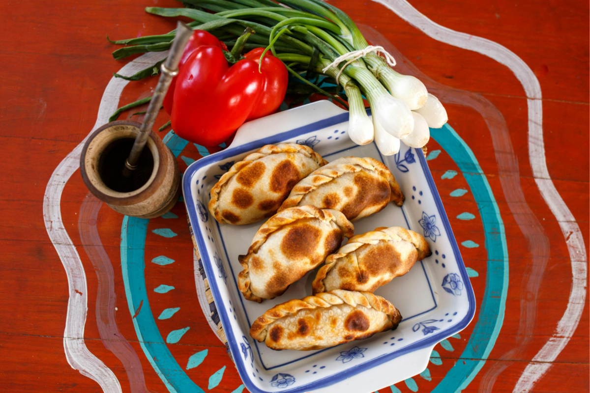 A colorful dish of baked empanadas alongside fresh veggies and mate.