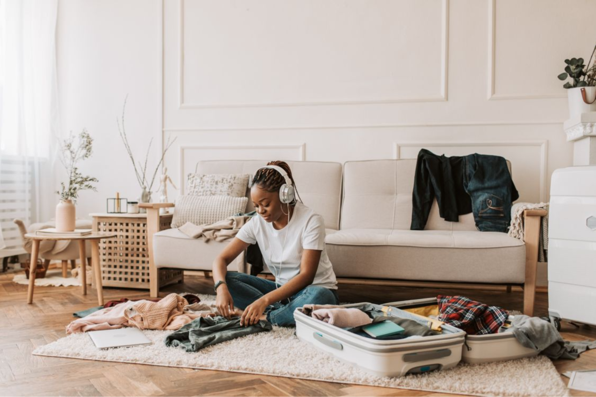 A woman packing a suitcase on the floor while wearing headphones.