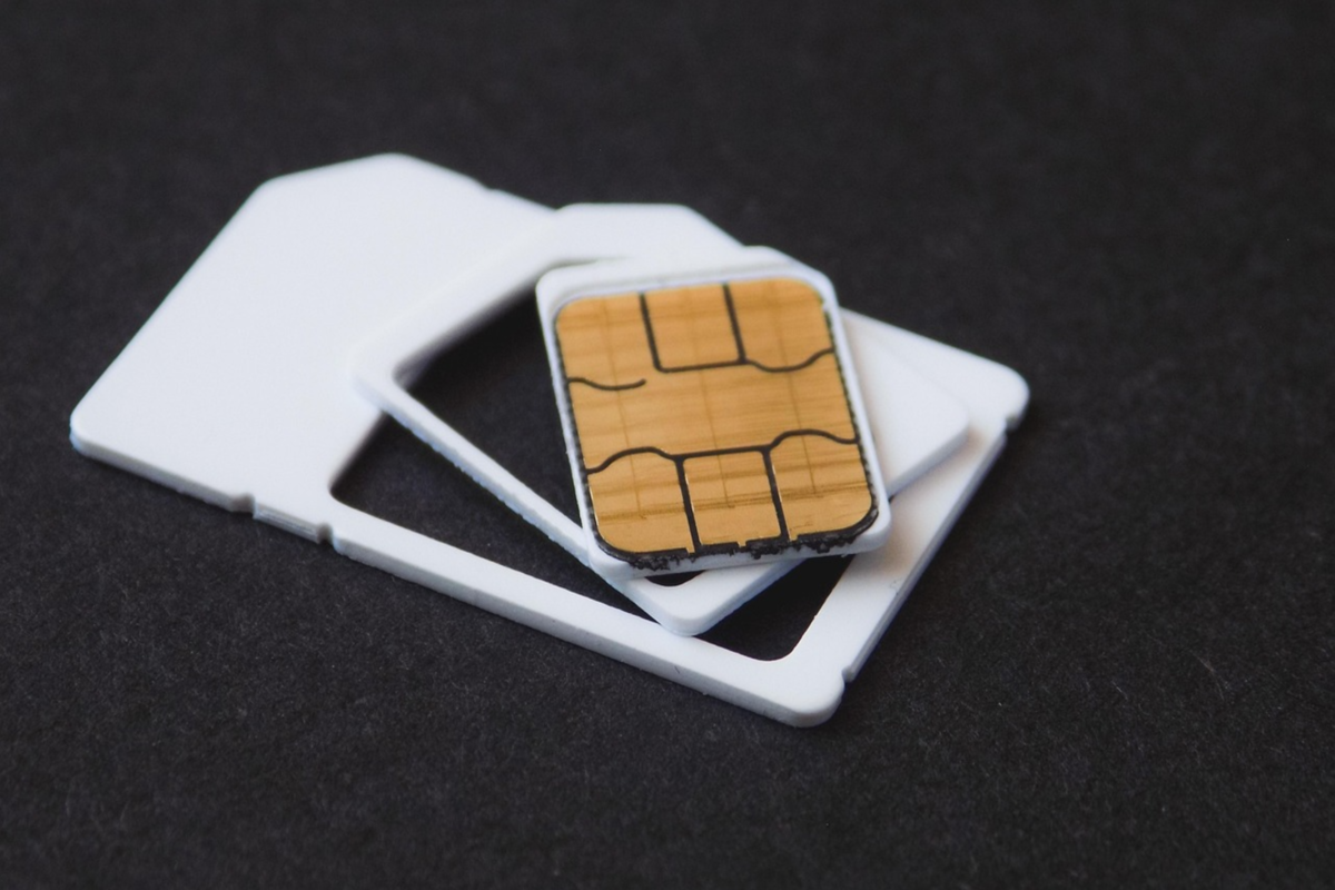 A close up of a nano SIM card, adapters for other card sizes, and eSIM ejector against a black background.