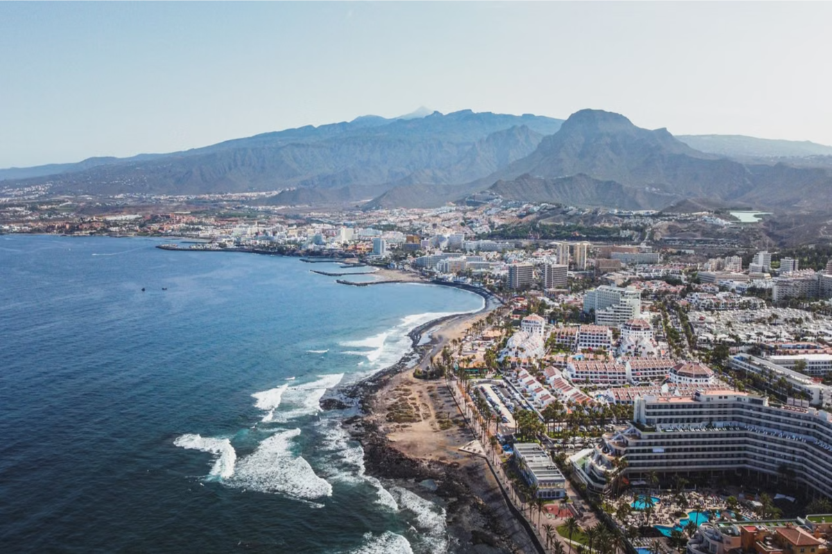 Sprawling Grand Canary coastline with beachfront resorts in the foreground and mountains in the background. 