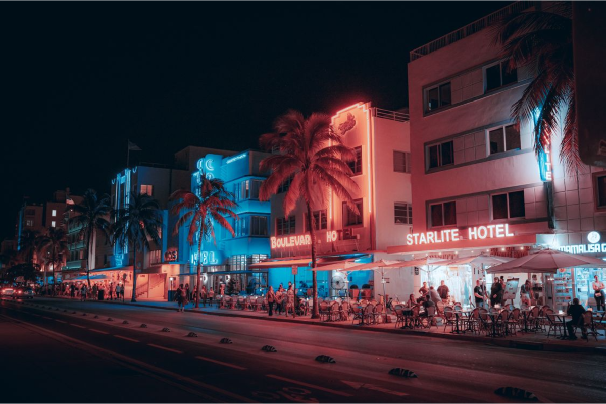 Ocean Drive at night with brightly lit neon signs and palm trees lining the street.