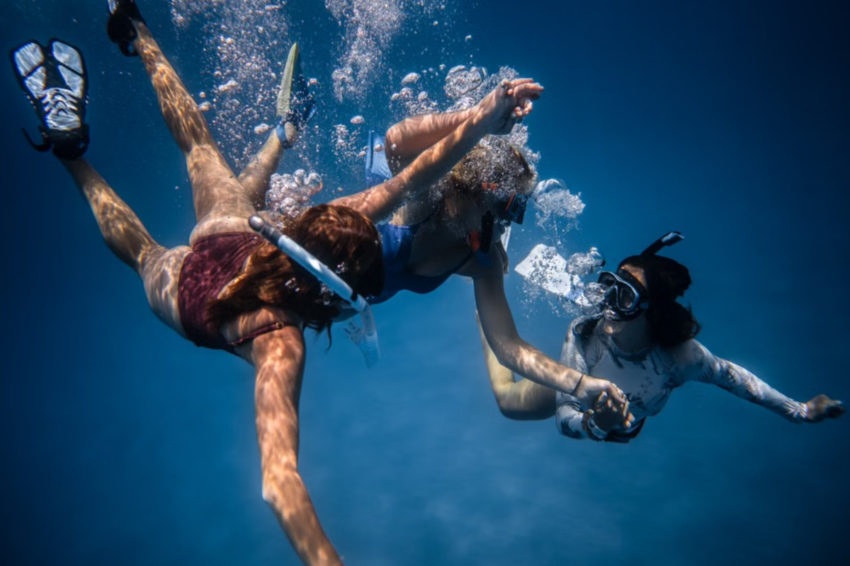 Three women holding hands while snorkeling.