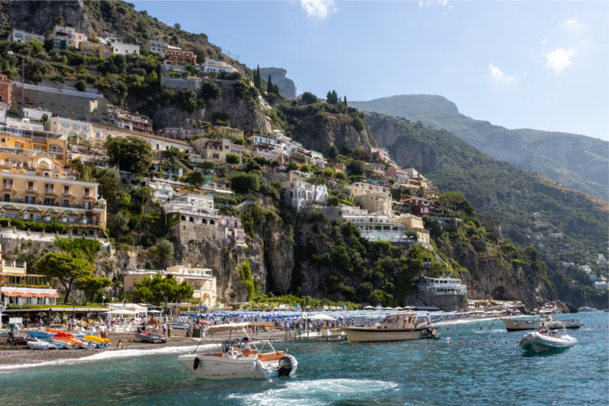 The Positano coastline with yachts in the foreground and buildings dotting the mountain face in the background.
